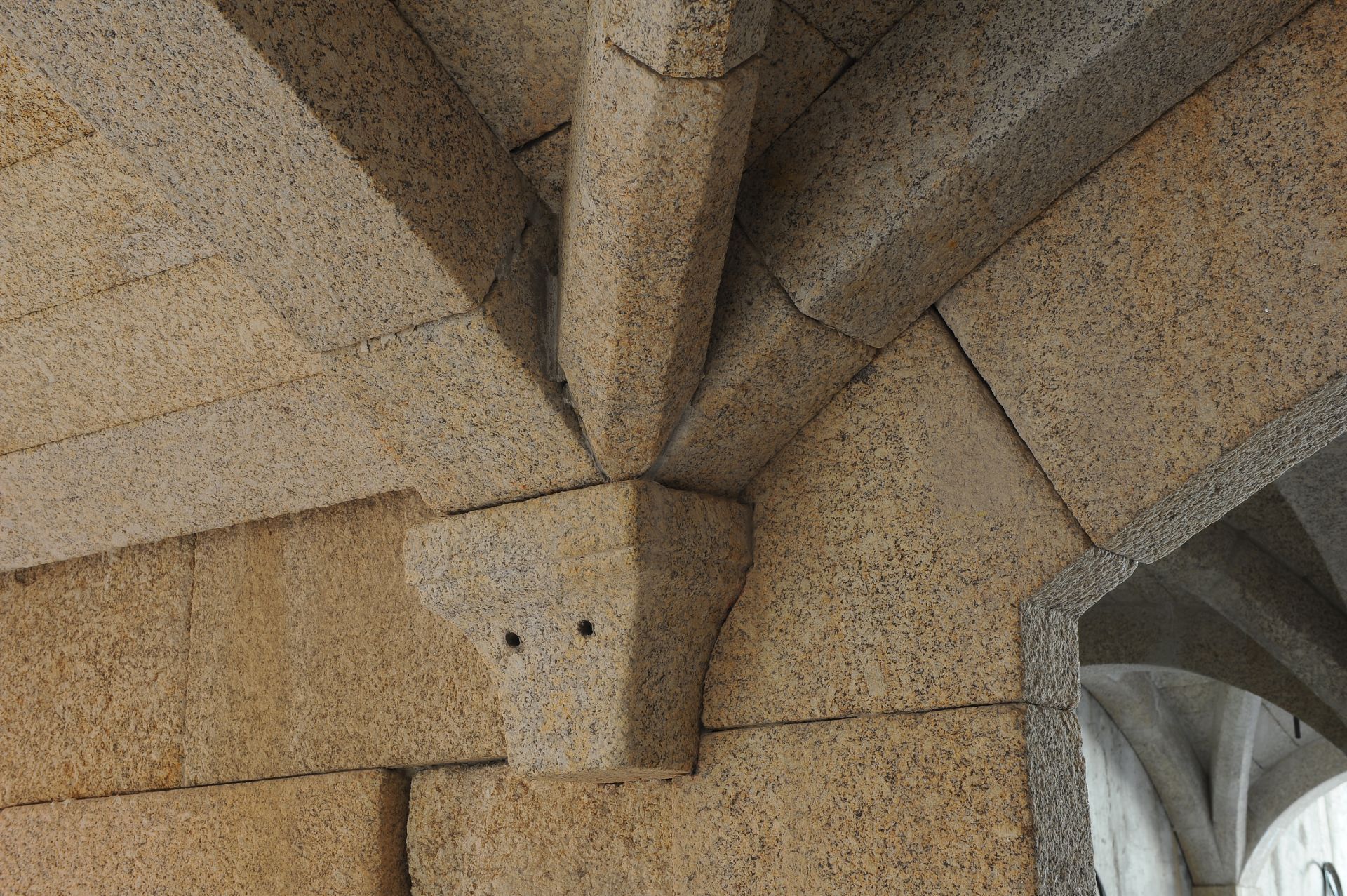 Una ménsula de piedra sostiene tres arcos de techo acanalados, hechos de bloques de granito texturizado de color marrón claro.