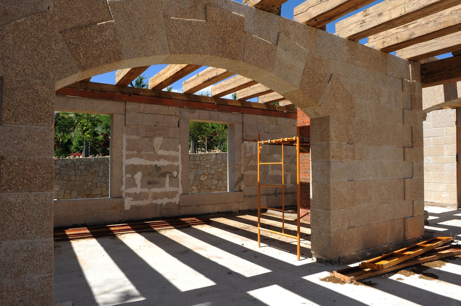Muros de piedra y un techo con vigas de madera en construcción en un espacio interior bañado por el sol.