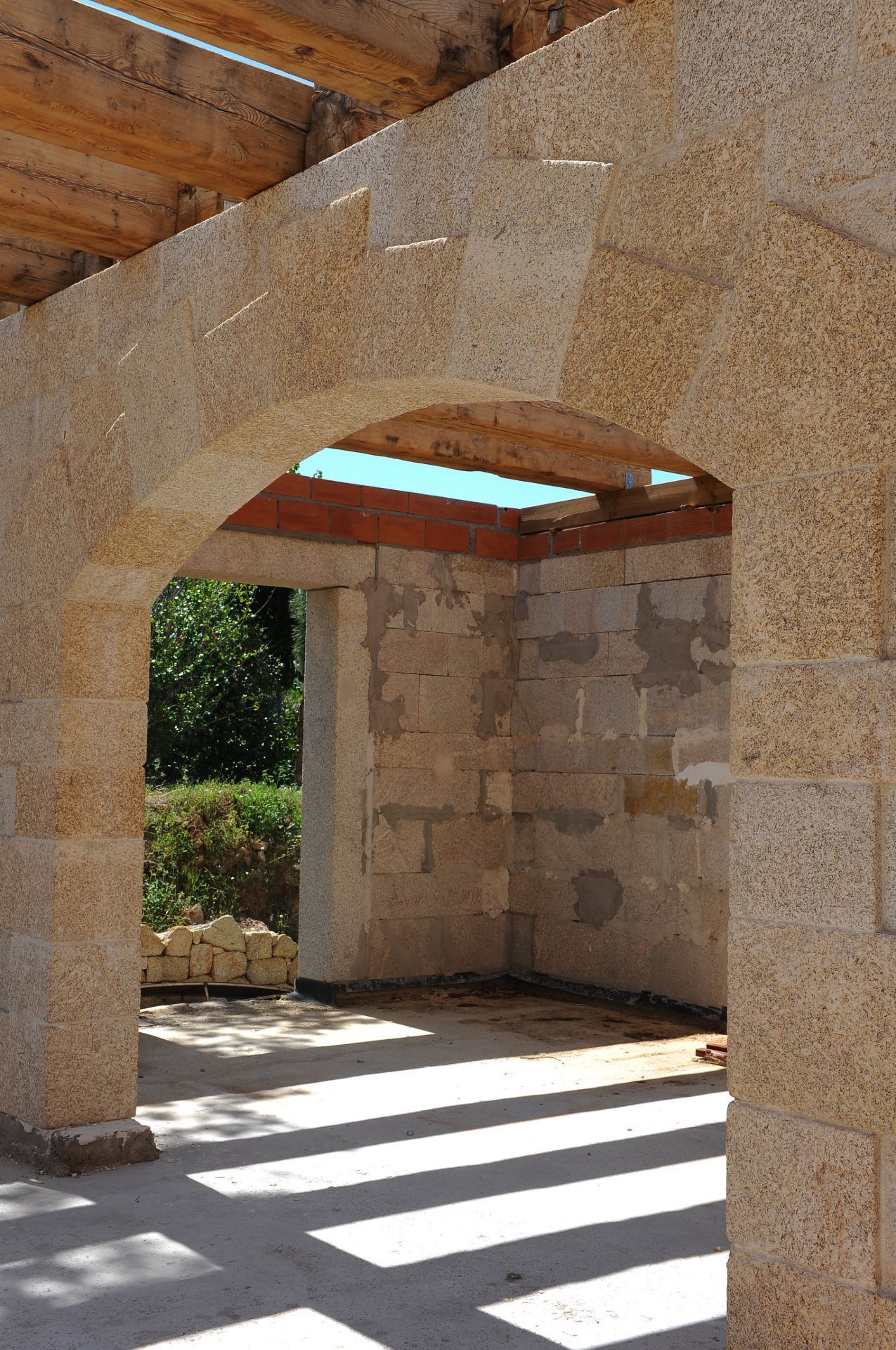 Un arco de piedra clara enmarca una habitación parcialmente construida con techo de vigas de madera y paredes de ladrillo.