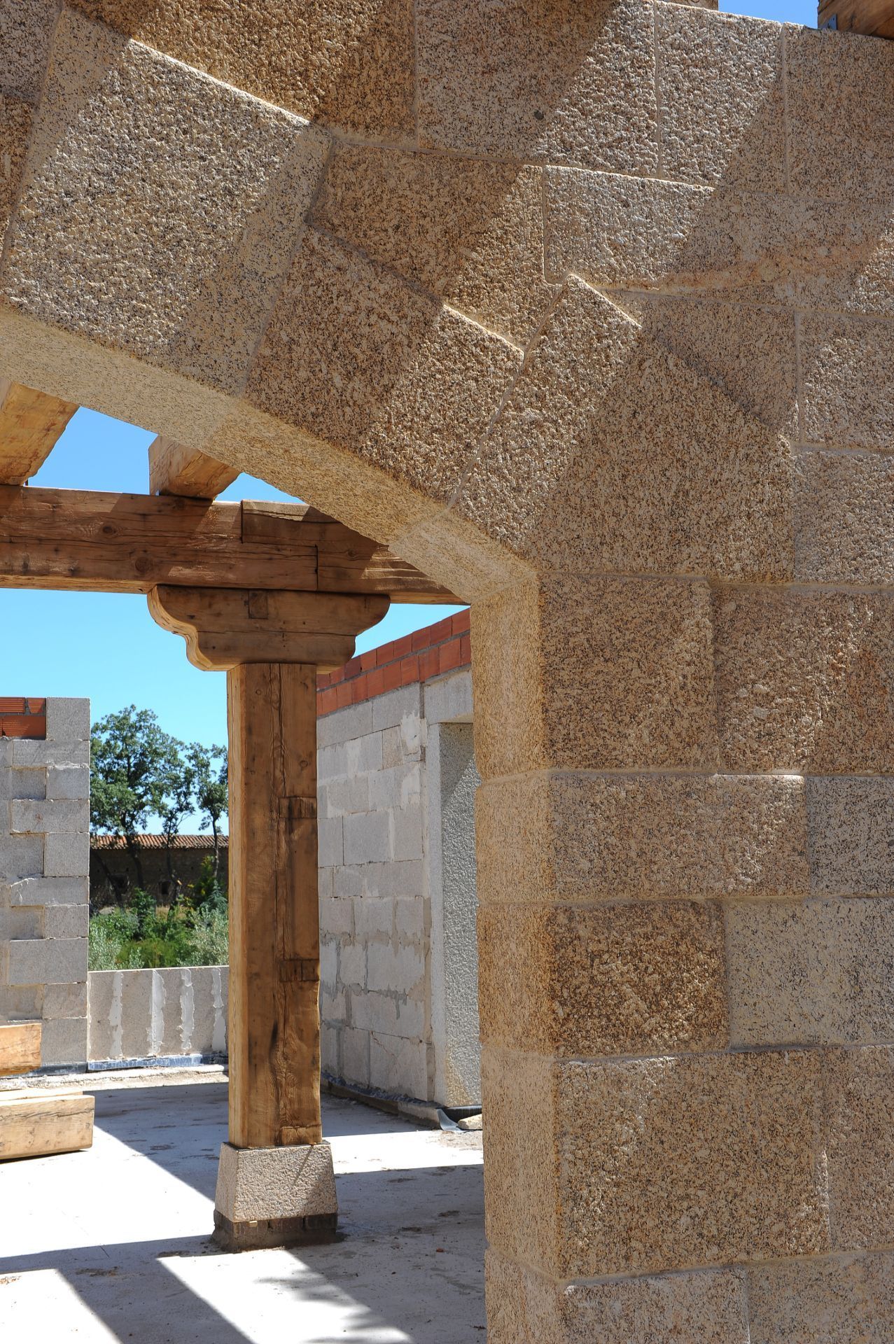 En primer plano se aprecia un arco de piedra con un pilar de soporte de madera y, al fondo, un edificio parcialmente construido.