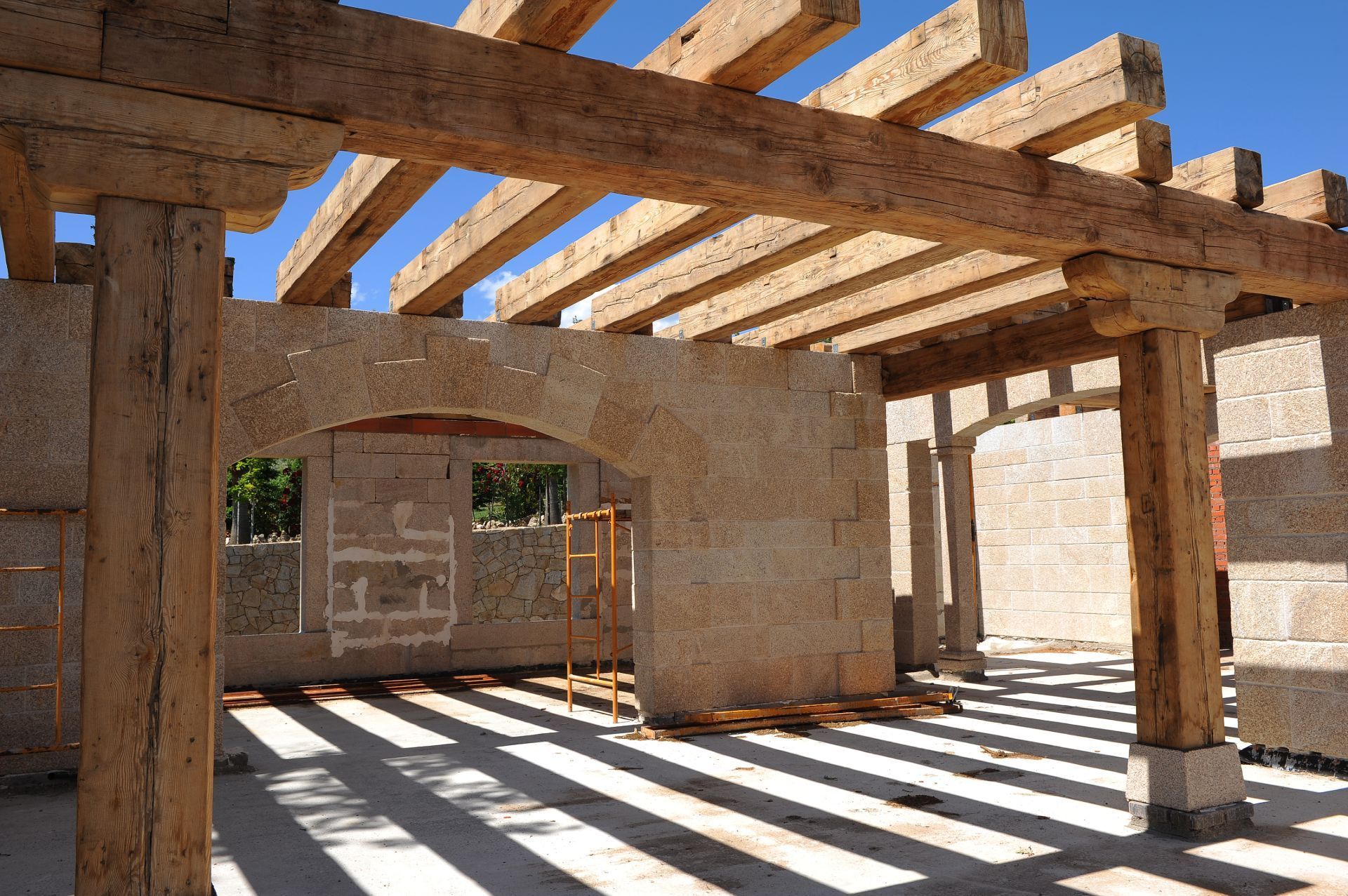 Una estructura de piedra sin terminar, con pesadas vigas de madera a la vista, bajo un cielo azul despejado.
