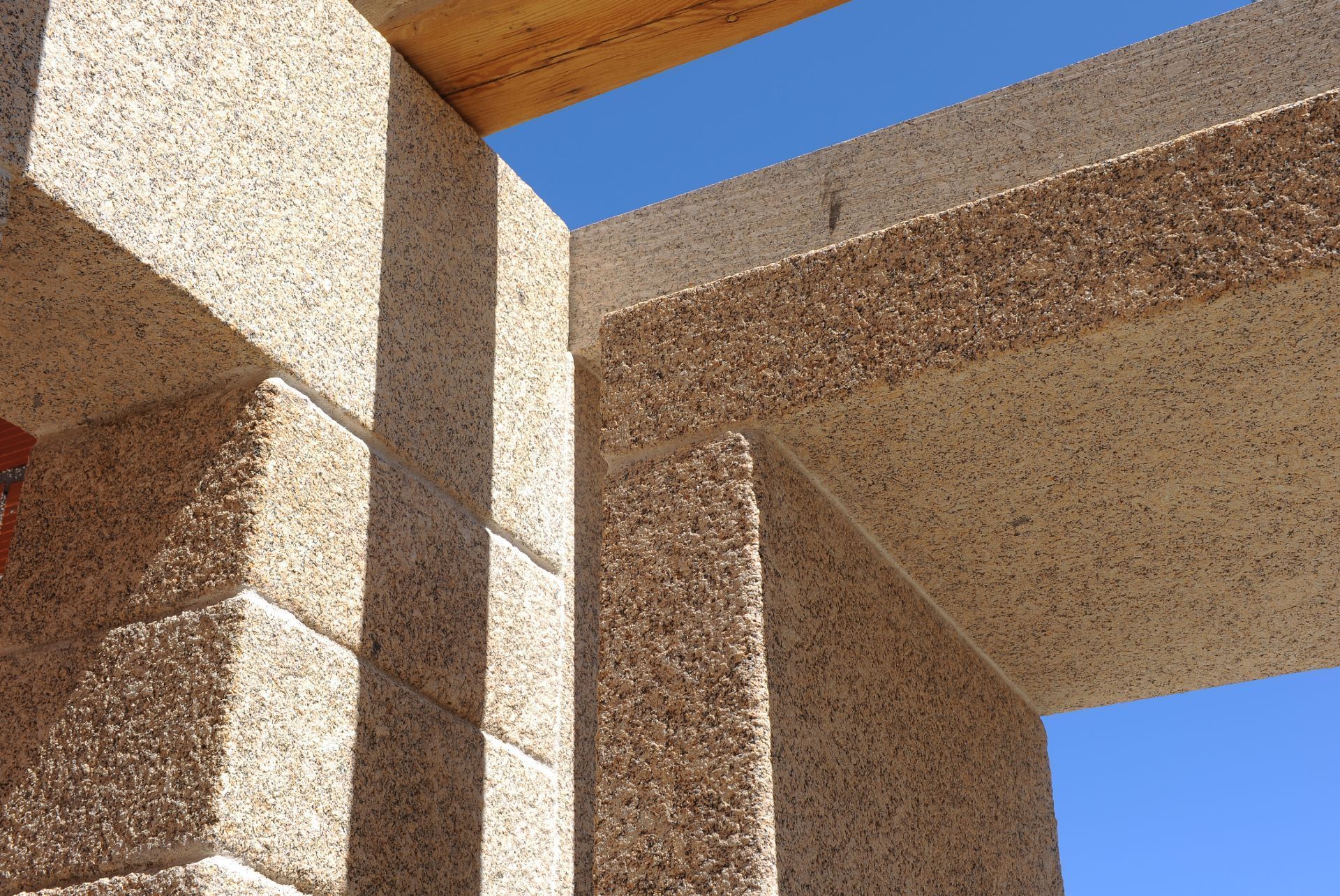 Vista desde un ángulo bajo de bloques de piedra de color tostado con textura, que forman una estructura en una esquina contra un cielo azul brillante.