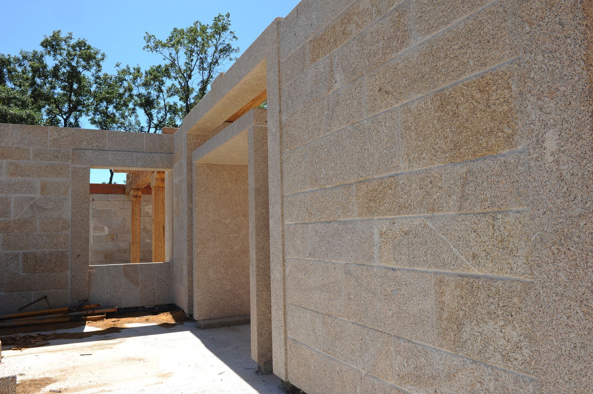 Construcción de un muro hecho de bloques de piedra texturizada de color claro con una puerta abierta y un marco de ventana.