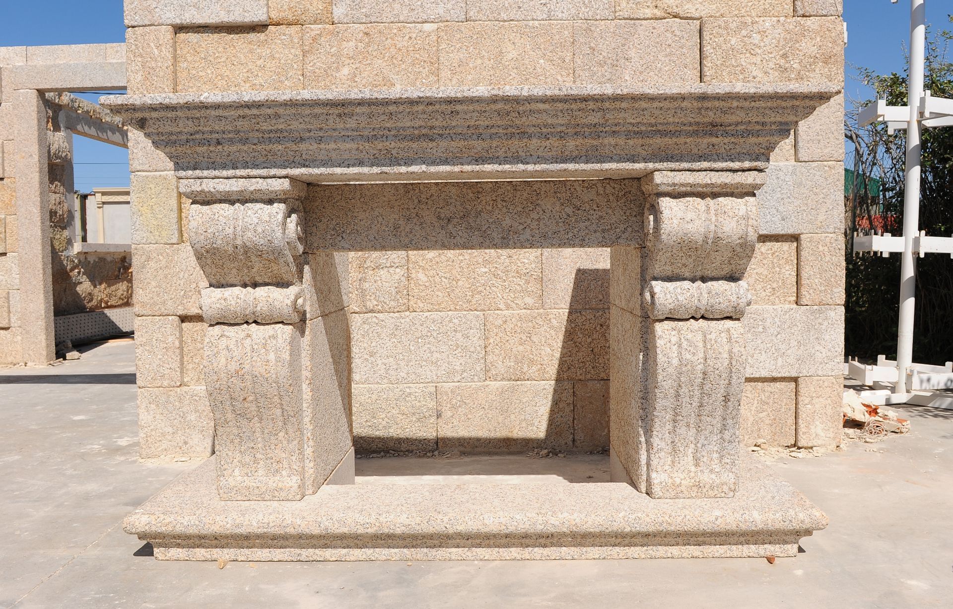 Una chimenea revestida de piedra beige con columnas decorativas y una repisa, colocada contra una pared de bloques de piedra a juego.