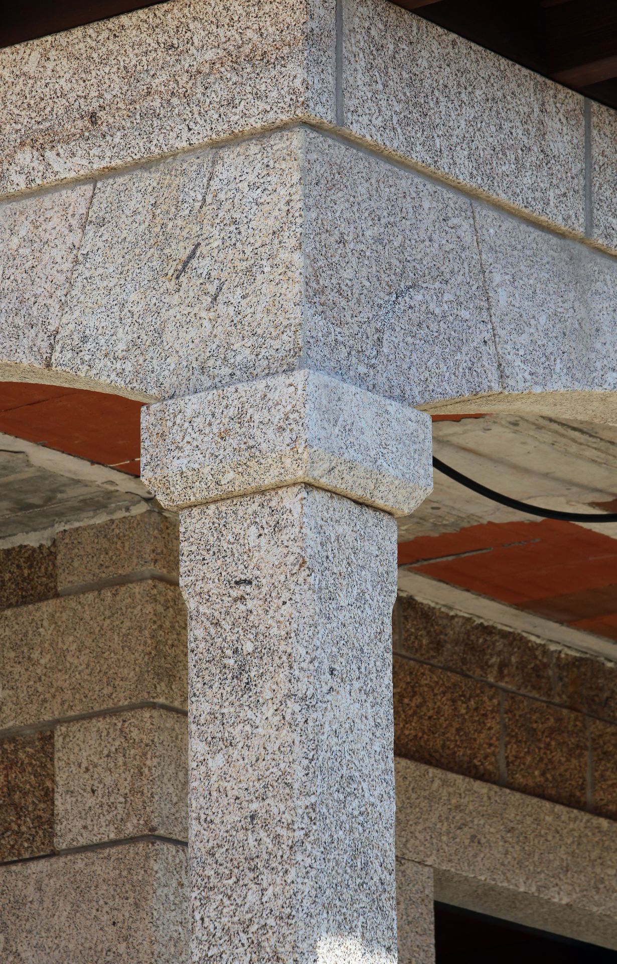 Primer plano de un pilar de granito moteado que sostiene una viga esquinera arquitectónica en el exterior.