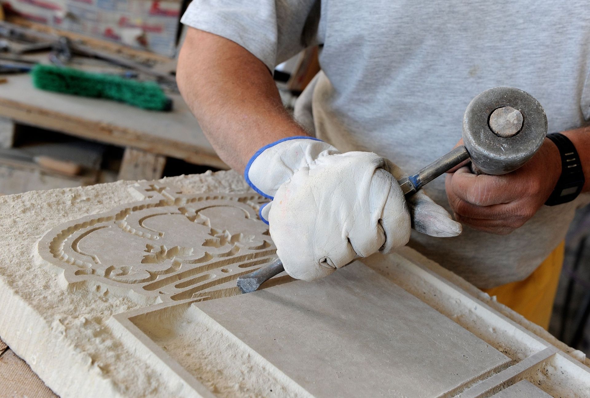 Una persona, con guantes puestos, talla el diseño de una corona en un bloque de piedra utilizando un martillo y un cincel.