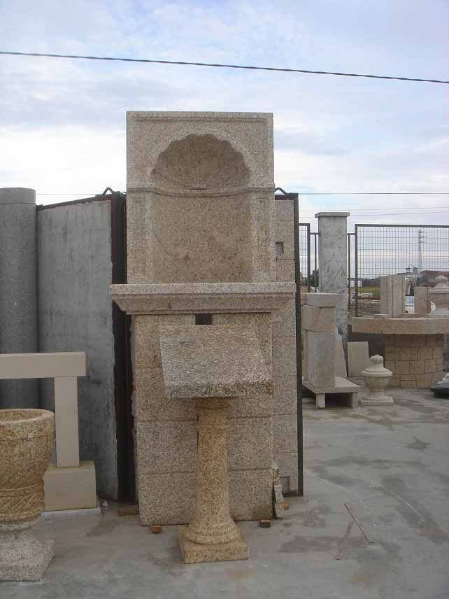 Una fuente de piedra con una hornacina en forma de concha y una pila sobre pedestal, expuesta en un patio de mampostería.