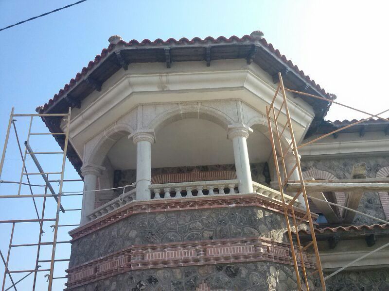 Un balcón de piedra en construcción con columnas arqueadas y detalles de azulejos, rodeado de andamios metálicos.