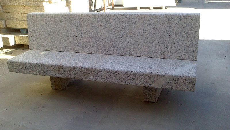 Un banco de piedra de color claro y moteado, con respaldo y dos robustas patas de apoyo, situado en una zona al aire libre.