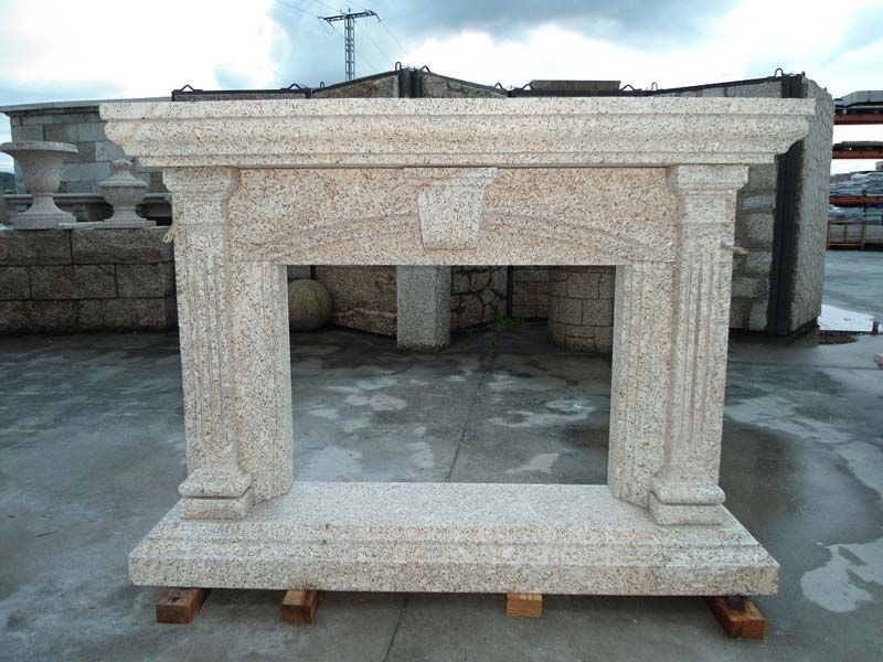 Una gran repisa de chimenea de granito de color claro con columnas estriadas y un diseño de clave de arco, expuesta en un patio exterior.