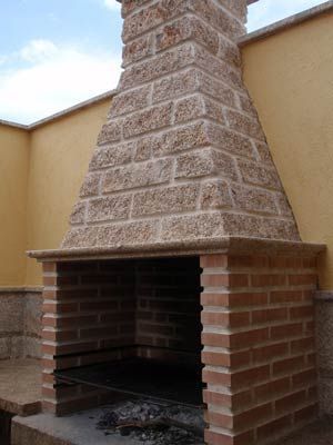 Una barbacoa de ladrillo para exteriores con una chimenea texturizada que imita la piedra, situada contra una pared de color beige.
