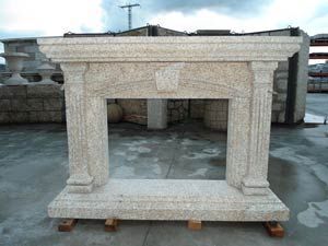 Una repisa de chimenea de piedra beige con columnas estriadas y un remate central, situada en un terreno pavimentado al aire libre.