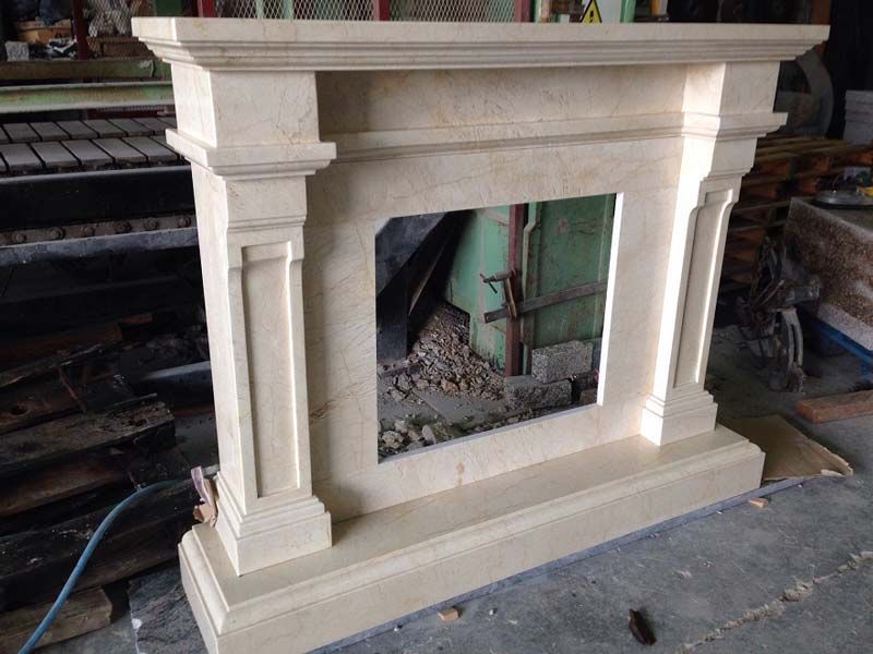 Una repisa de chimenea de piedra de color claro, ubicada en un taller, que muestra una abertura rectangular y una arquitectura clásica.