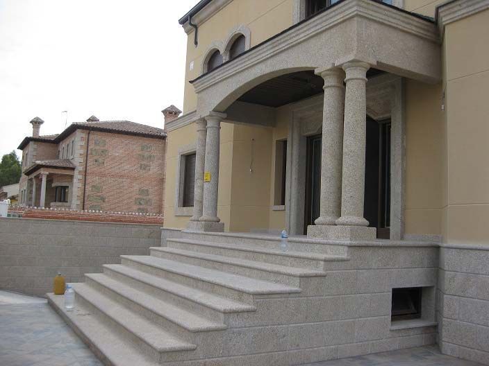 Una entrada a la casa de color tostado con un pórtico de columnas de piedra y una amplia escalera de granito que conduce a la puerta principal.