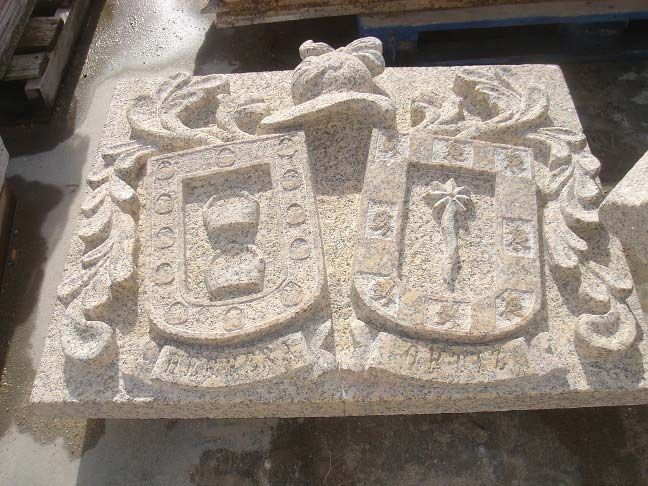 Una escultura de piedra que representa dos escudos heráldicos uno al lado del otro, con emblemas simbólicos, enmarcados por follaje ornamentado y un casco.
