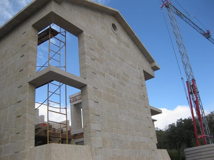 Un edificio de color beige, construido con bloques de piedra, en construcción, con un alto andamio metálico dentro de una gran abertura de ventana y una grúa.
