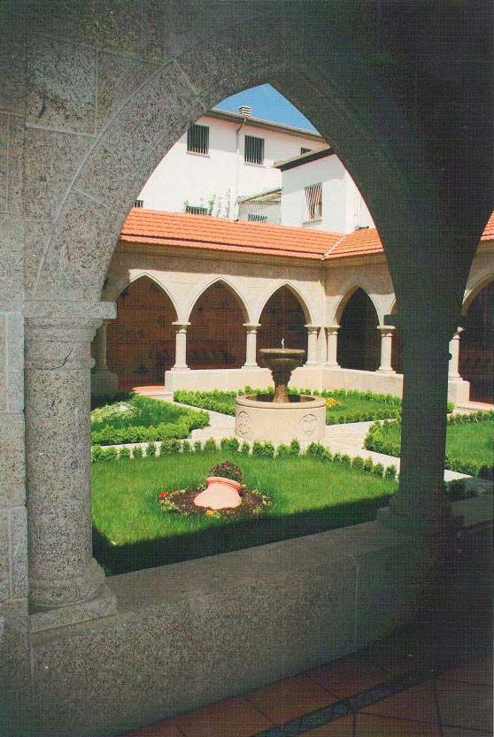 Un claustro de piedra con arcadas enmarca un patio central con césped verde bien cuidado, setos bajos de boj y una fuente de piedra.