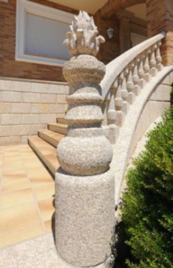 Un poste de piedra rematado con un adorno decorativo se alza junto a una escalera curva con balaustrada de piedra.