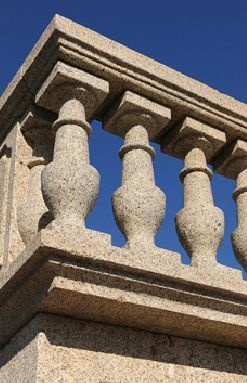 Primer plano de una balaustrada de granito desgastado por el tiempo contra un cielo azul brillante.
