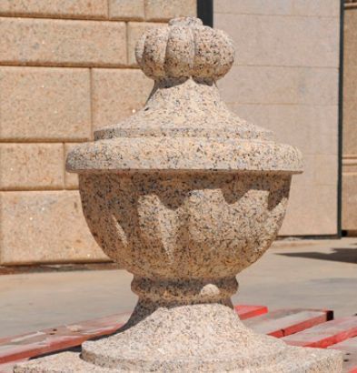 Remate de piedra de granito beige con tallas decorativas, que presenta una parte superior estriada y una base en forma de urna.