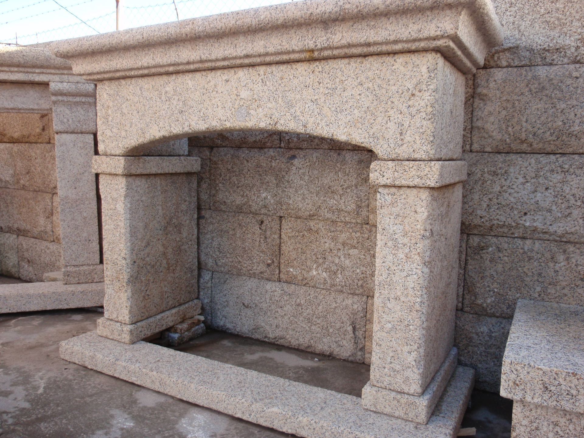 Una repisa y hogar de chimenea de piedra para exteriores, hechos de granito beige moteado, ubicados en un patio de exhibición industrial.