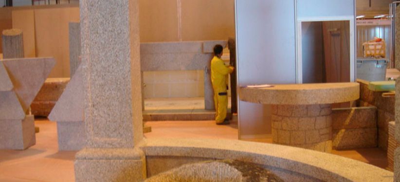 Un trabajador con uniforme amarillo instala paneles de piedra en un estudio o galería repleto de formas arquitectónicas de piedra.