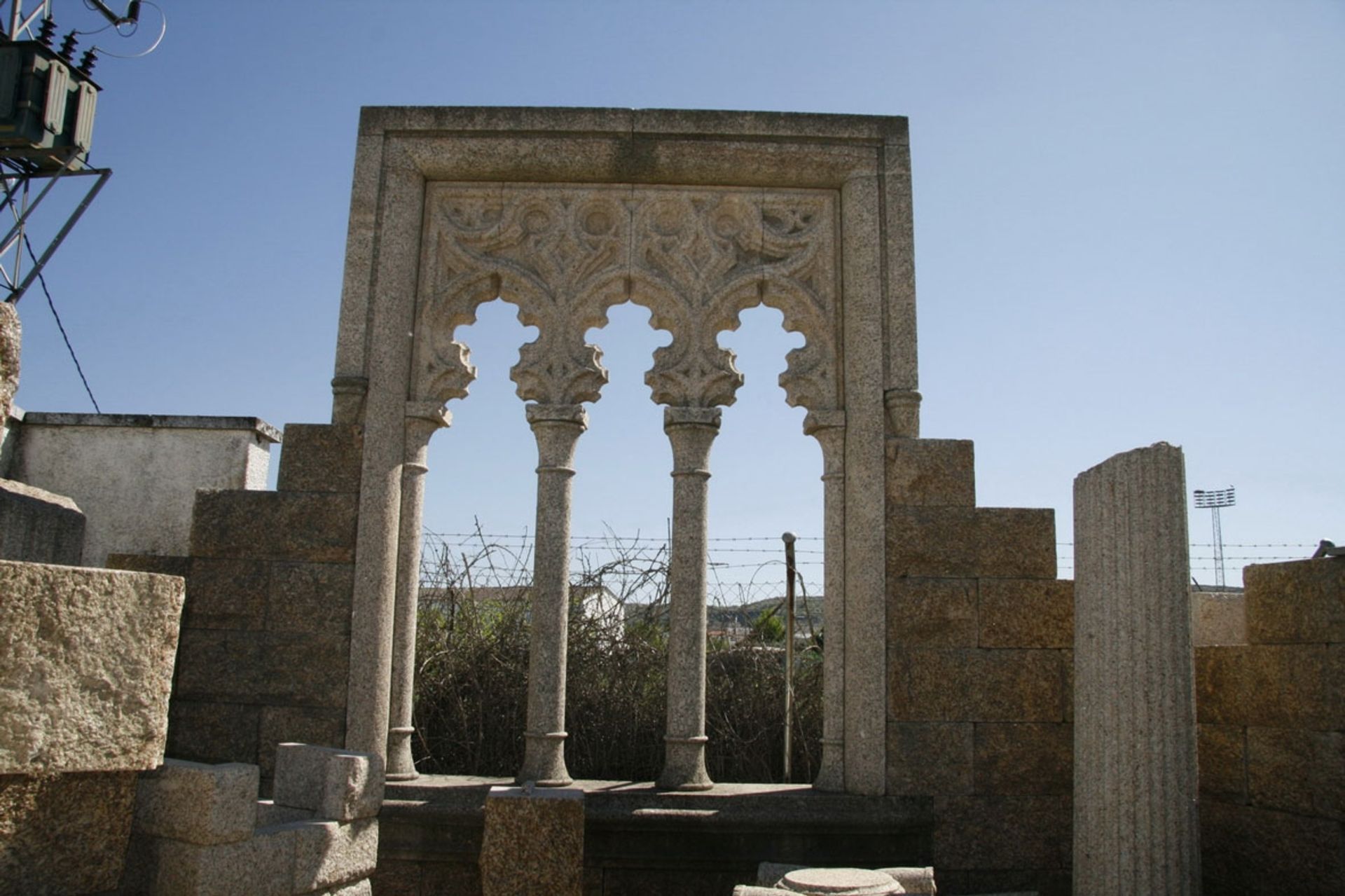 Un arco de piedra con tres pequeños arcos polilobulados tallados, sostenidos por columnas, enmarcado por un cielo brillante y despejado.