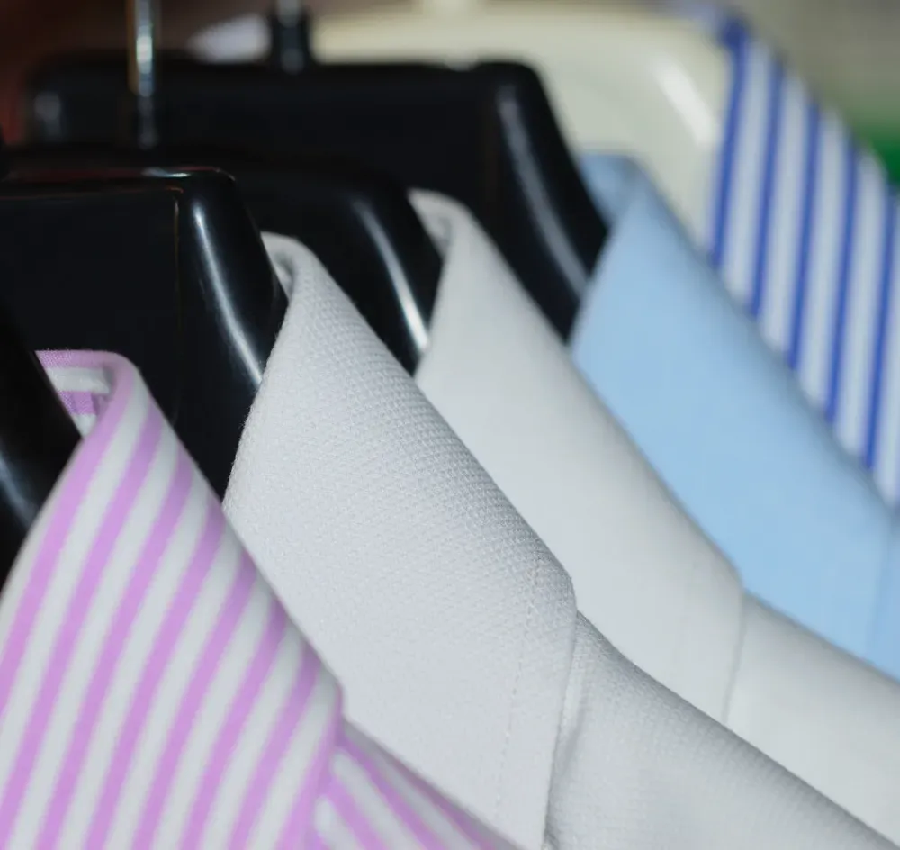 Primer plano de camisas con cuello en varios colores y rayas colgadas en perchas negras.