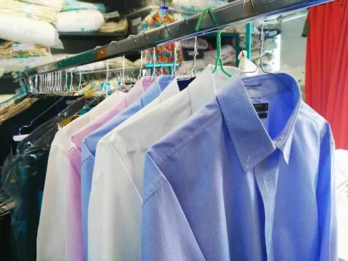 Camisas en perchas en una tintorería, varios colores pastel: rosa, azul, blanco.