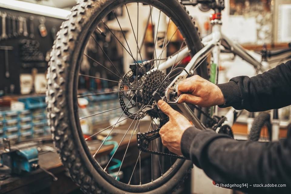 Die Hände eines Mechanikers justieren die Zahnräder an einem Mountainbike-Rad in einer Werkstatt.