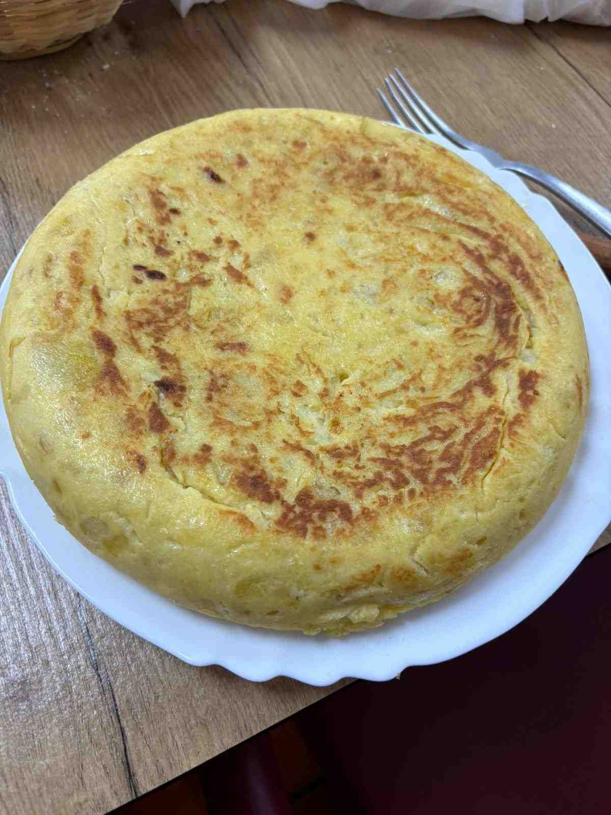 Pastel redondo de color marrón dorado sobre un plato blanco en una mesa de madera con un tenedor cerca.