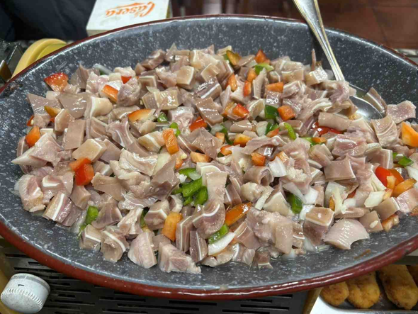 Mariscos y verduras cortados en dados, servidos en una fuente ovalada negra con una cuchara para servir.