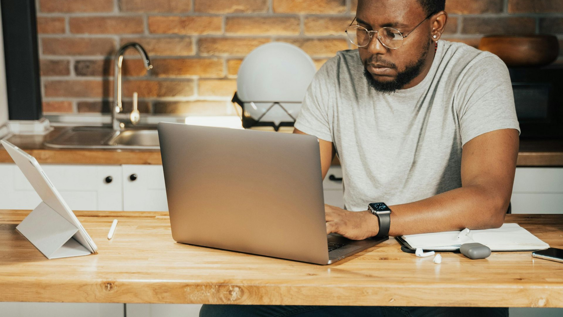 Un señor viendo un ordenador sentado en su cocina.