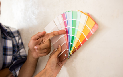 Une personne montre du doigt un échantillon de peinture rose tenu contre un mur, avec d'autres échantillons de couleurs disposés en éventail.