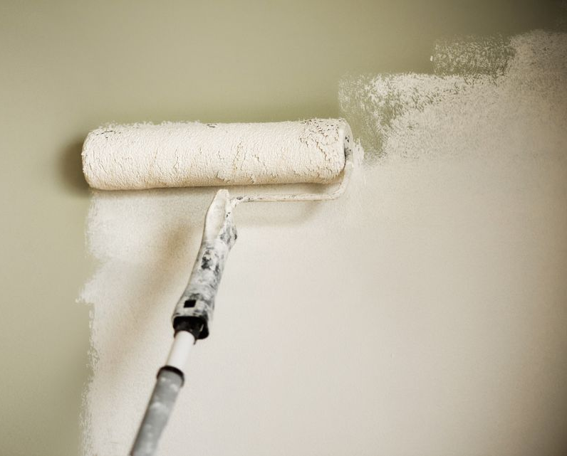 Un rouleau à peinture appliquant de la peinture blanche sur un mur vert.