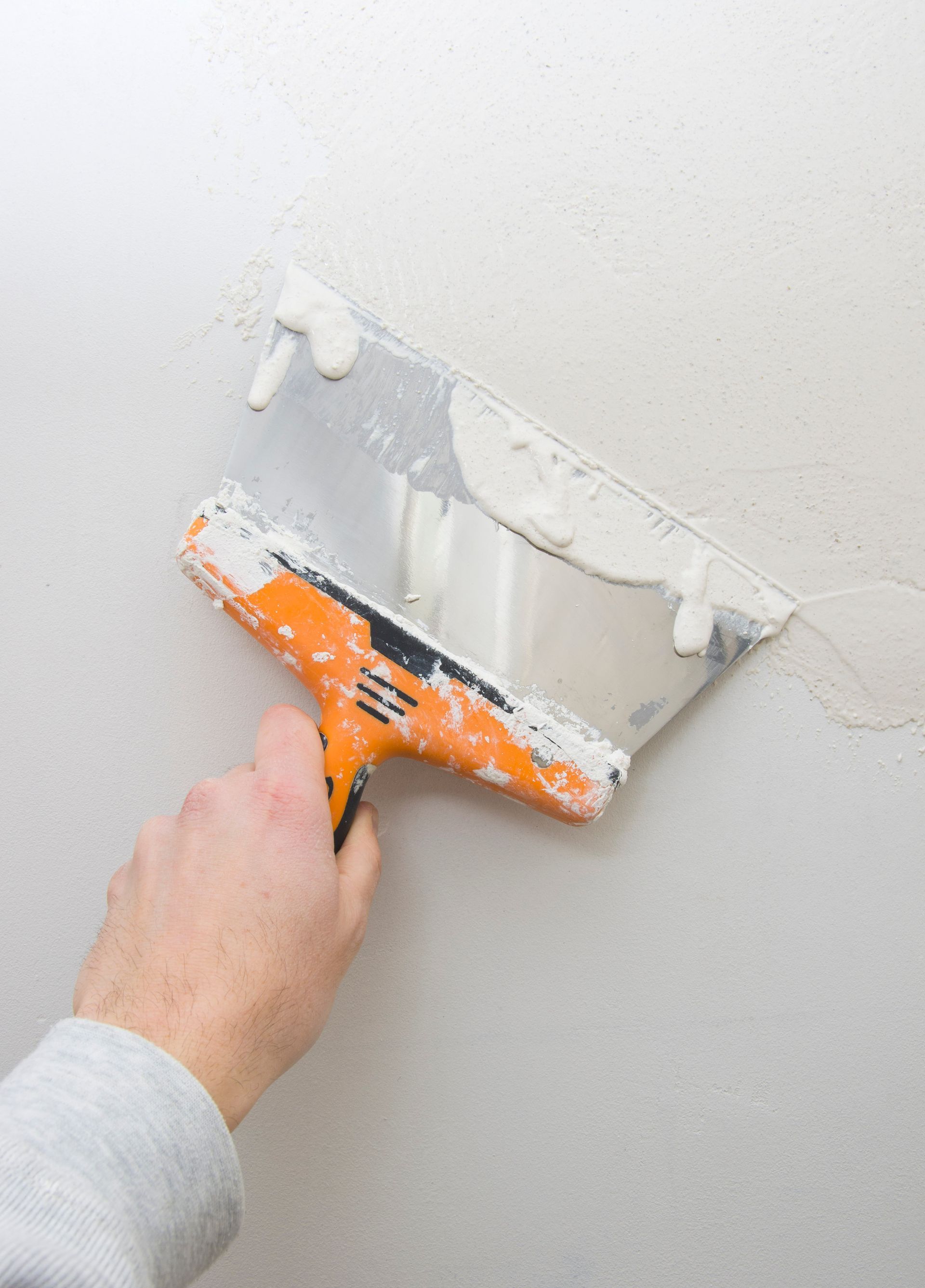Personne utilisant une truelle pour appliquer du plâtre blanc sur un mur ; outil orange et argenté.