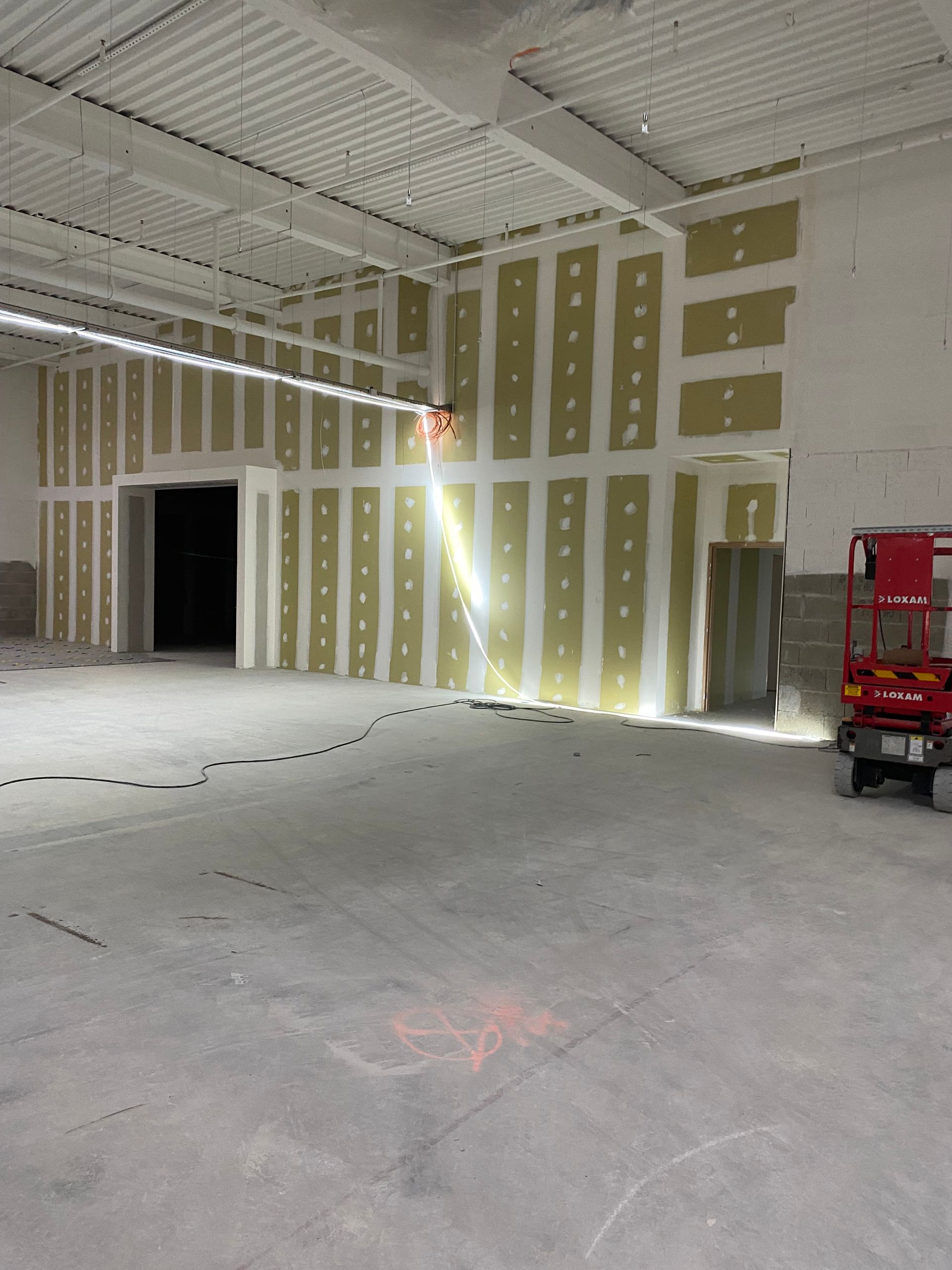 Une personne utilise un couteau à mastic pour appliquer du composé mural afin de réparer les dommages sur un mur gris clair.