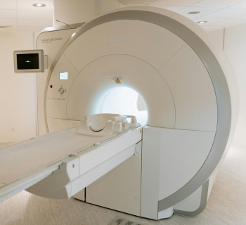 Aparelho de ressonância magnética em uma sala branca; a cama se estende para dentro da abertura circular.
