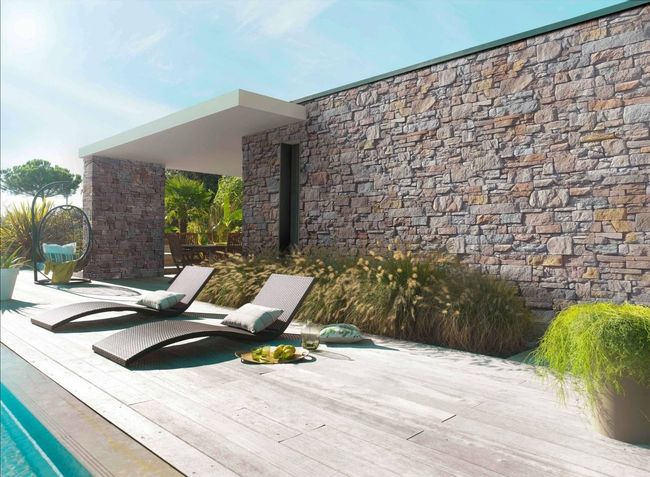 Terrasse ensoleillée au bord de la piscine avec deux chaises longues le long d'un muret en pierre.