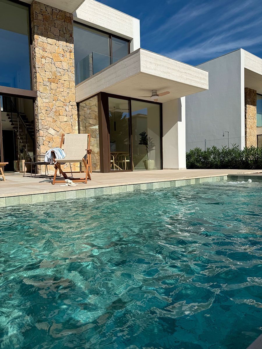 Maison moderne avec chaises au bord d'une piscine turquoise sous un ciel bleu