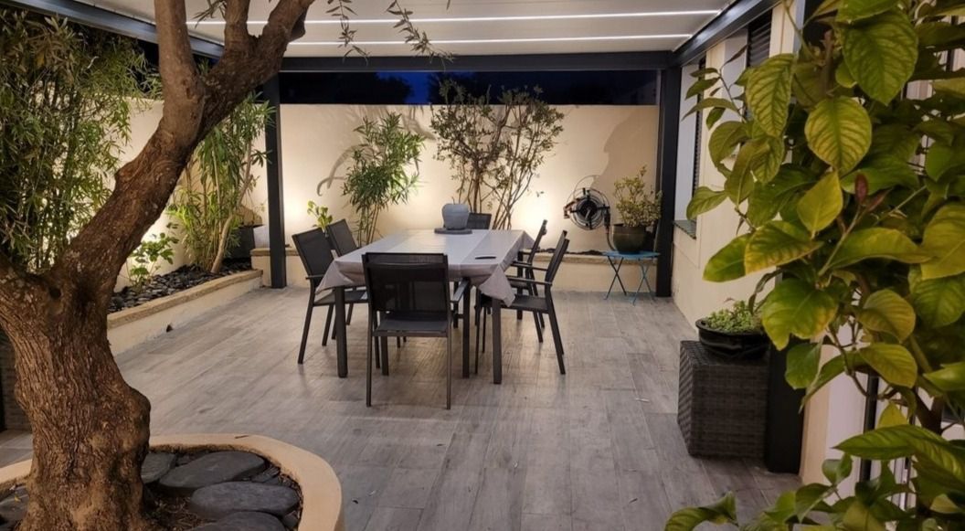 Terrasse extérieure avec table et chaises, entourée de plantes en pot.