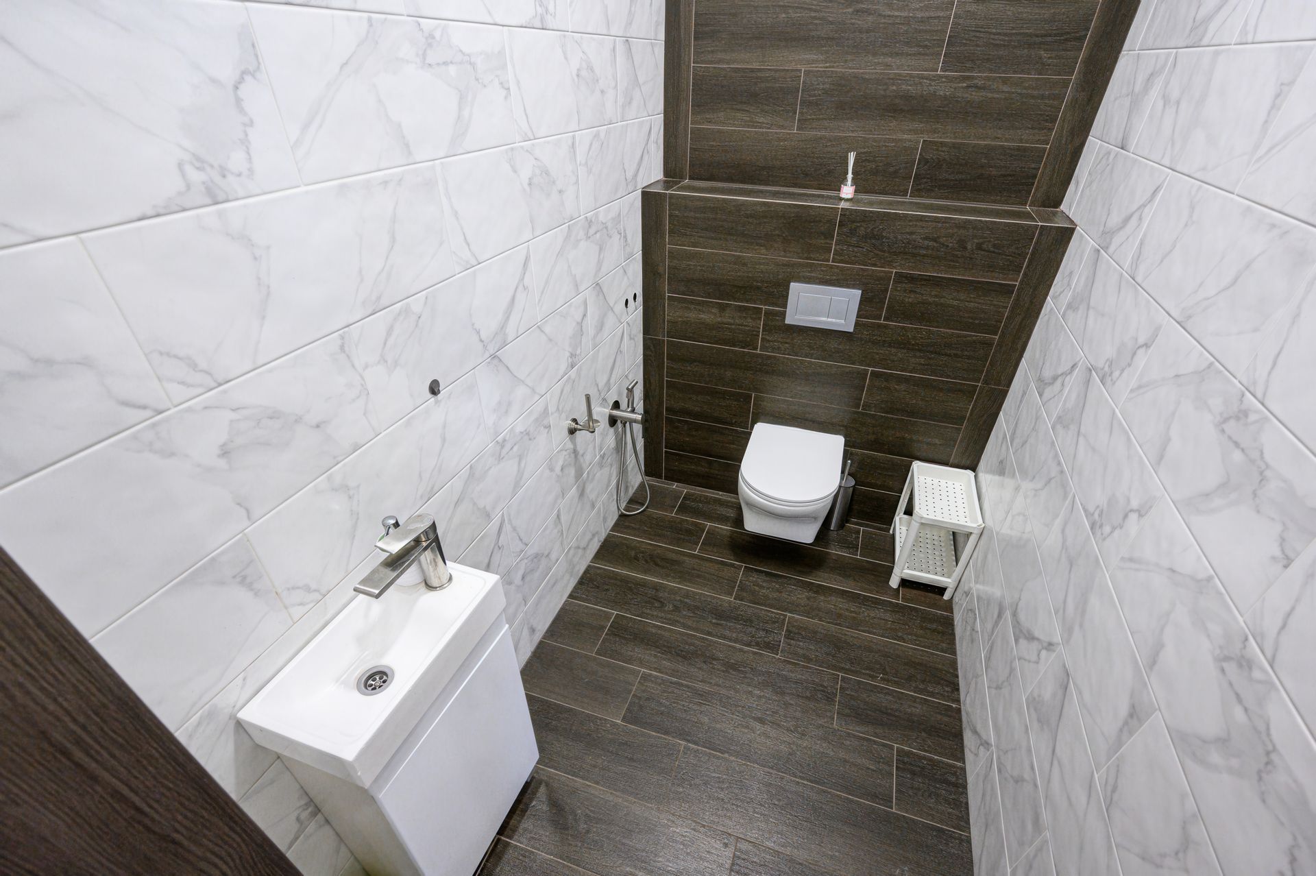 Petite pièce carrelée avec murs en marbre blanc, sol foncé, lavabo et toilettes.