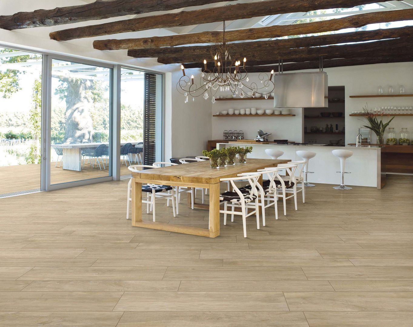 Salle à manger lumineuse et ouverte avec table en bois, chaises blanches, poutres apparentes et grandes portes vitrées.