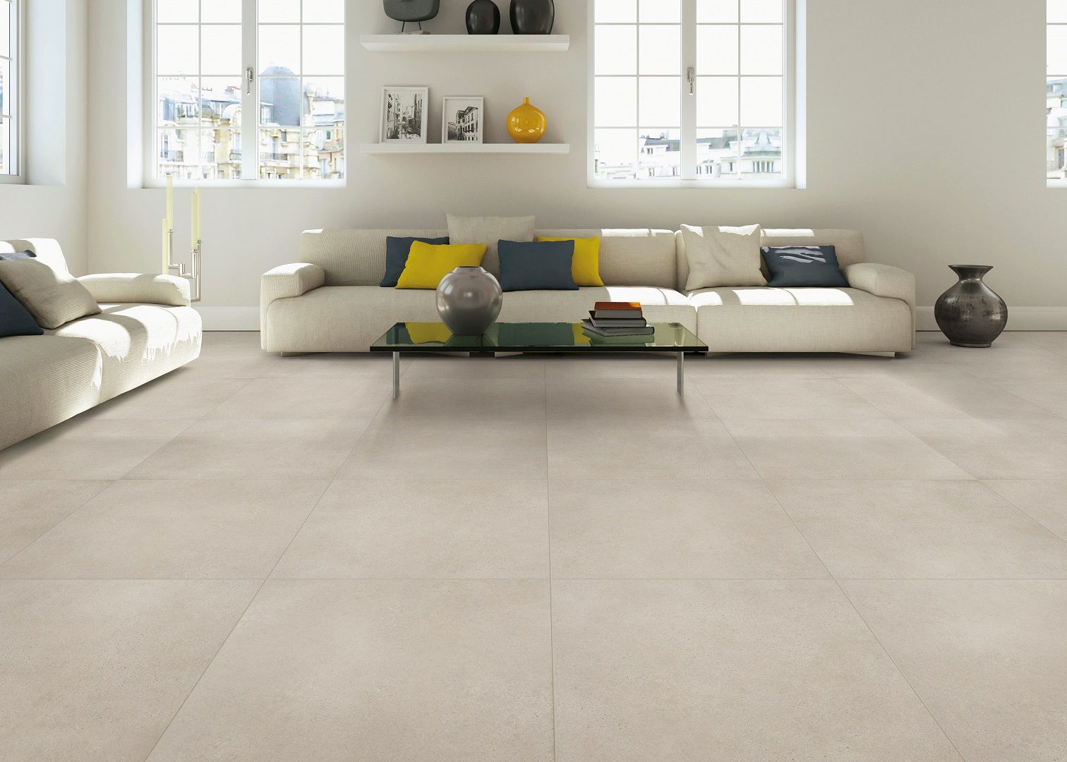 Salon lumineux avec canapés blancs, table basse en verre et grandes fenêtres donnant sur un sol carrelé beige