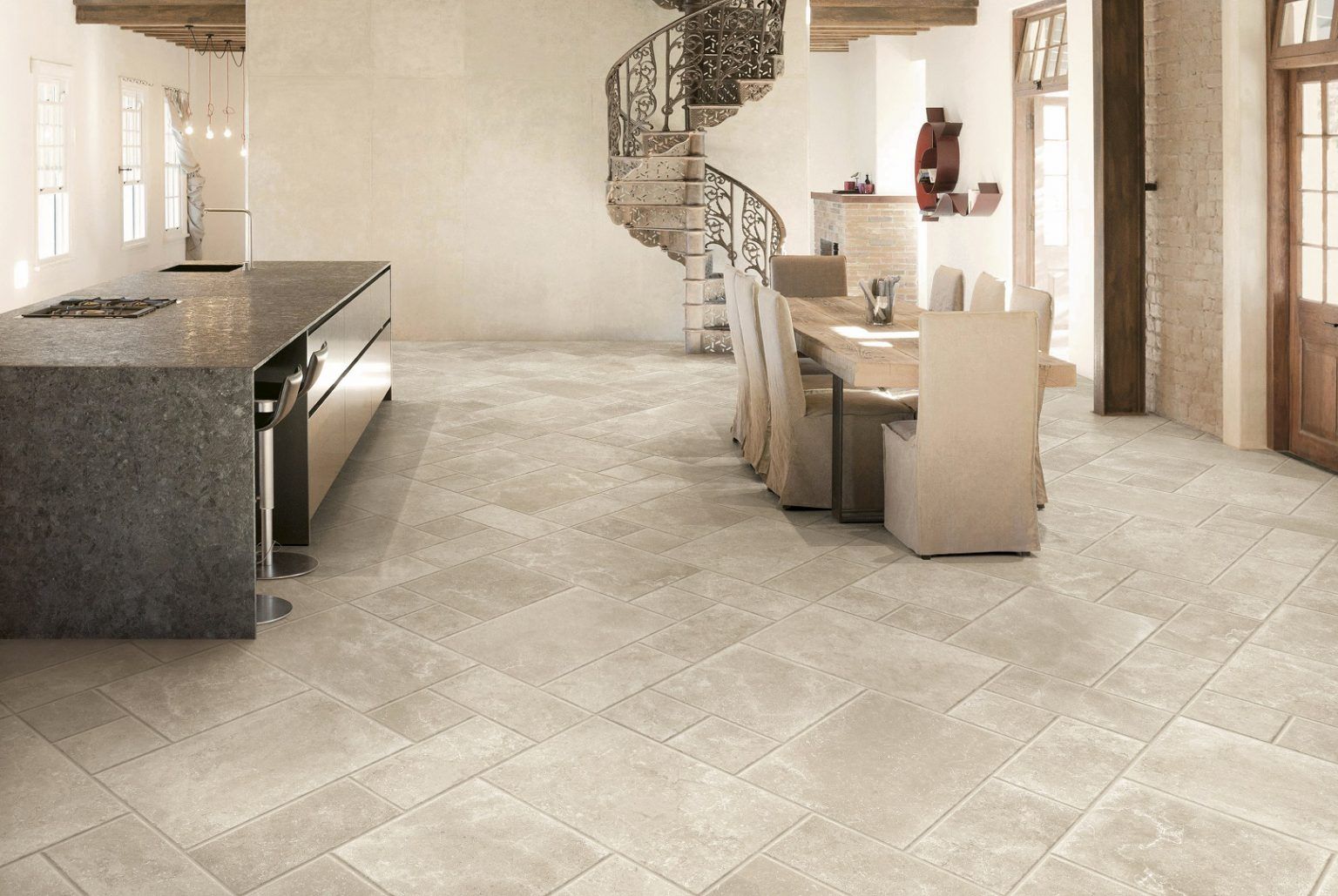 Cuisine moderne avec sol carrelé beige, îlot en granit et escalier en colimaçon dans un espace ouvert et lumineux