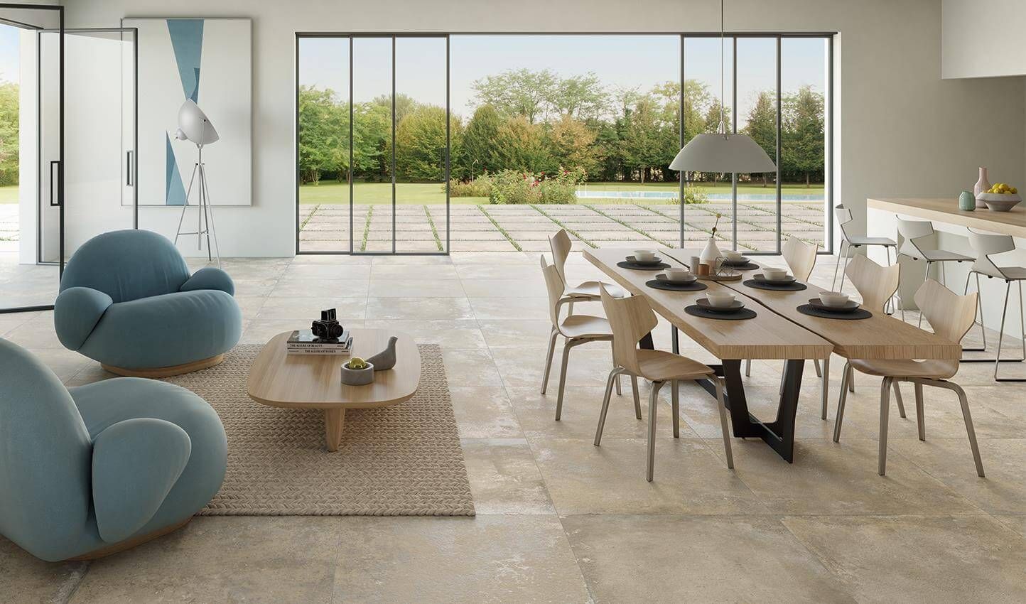 Salle à manger moderne et ouverte avec de grandes fenêtres, des fauteuils bleus et une table dressée pour un repas.
