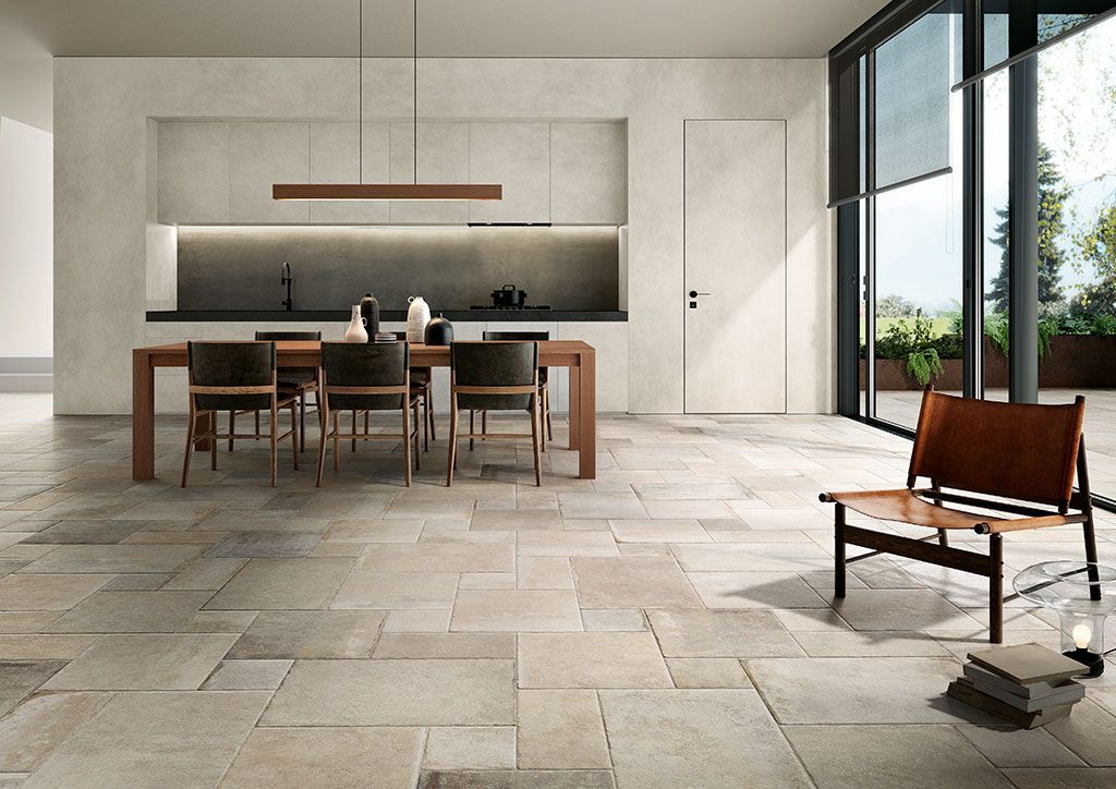 Salle à manger moderne et minimaliste avec table et chaises en bois, sol en pierre et grandes fenêtres.