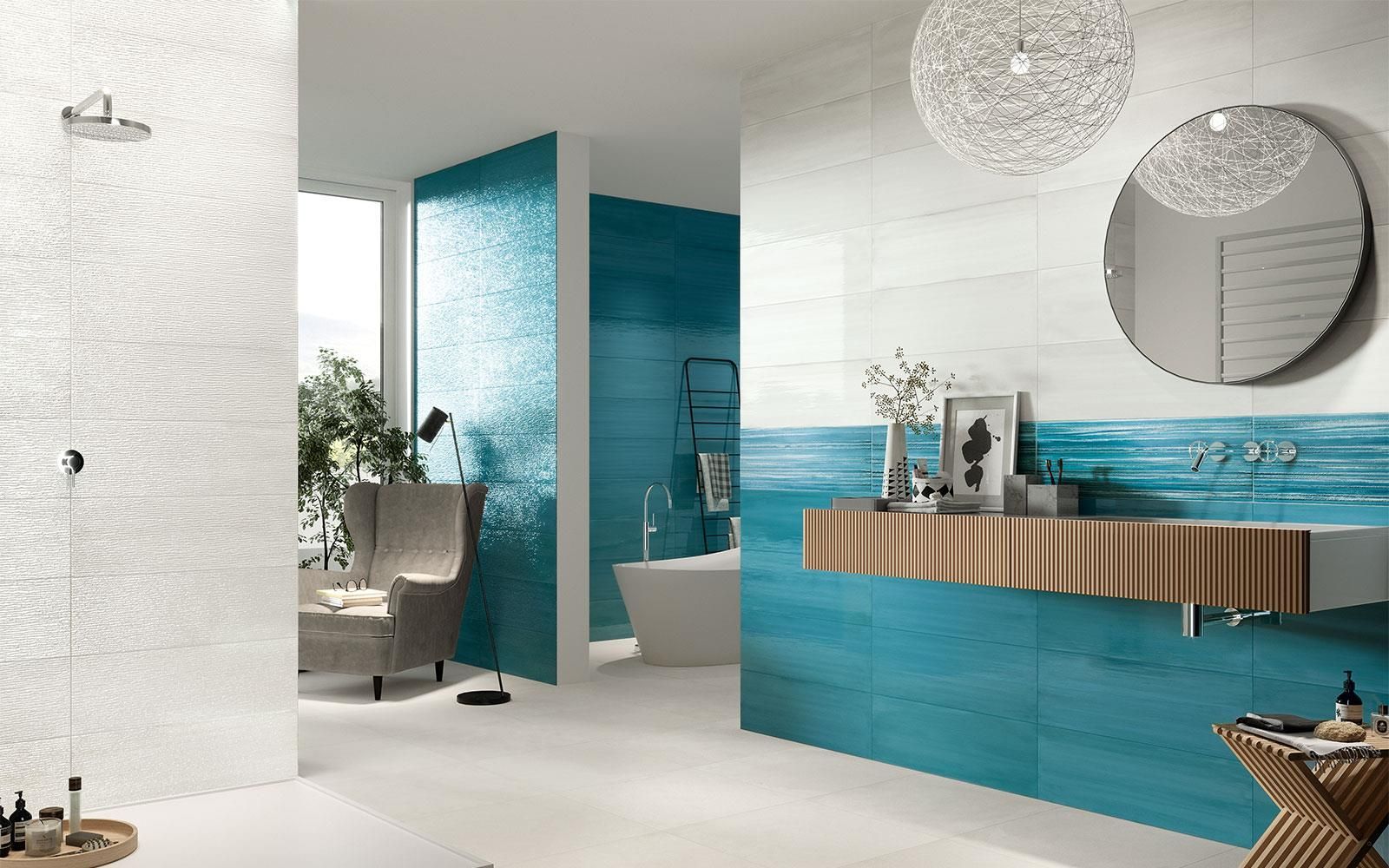 Salle de bains moderne blanche avec carrelage turquoise, meuble lavabo suspendu en bois, miroir rond et suspensions lumineuses.