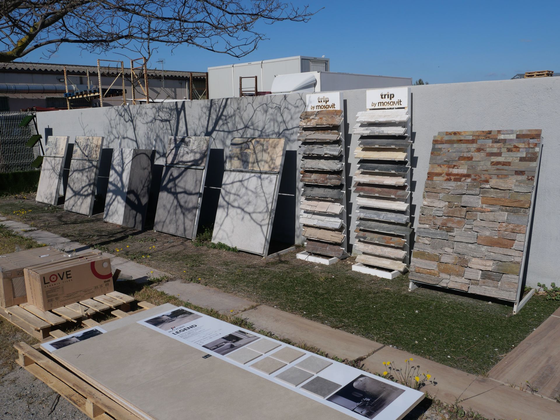 Présentation extérieure de grandes dalles de pierre et de carrelage appuyées contre un mur dans une cour