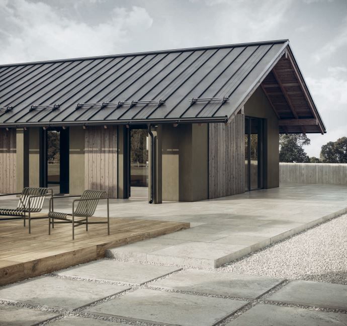 Maison moderne avec toit en métal, chaises de patio et grande terrasse en béton extérieure